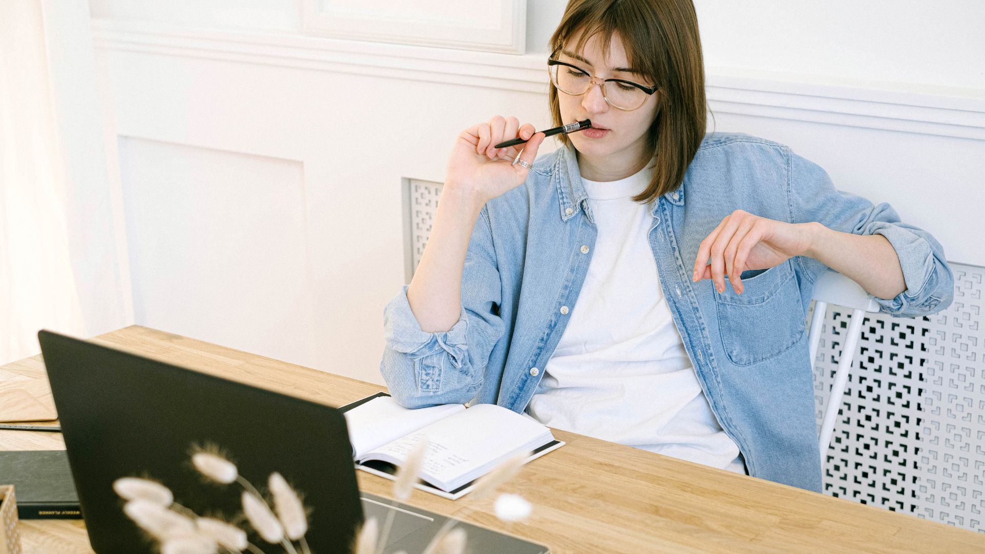 A manager is sitting at a table with her laptop and notebook, thinking hard about how to give clear feedback.