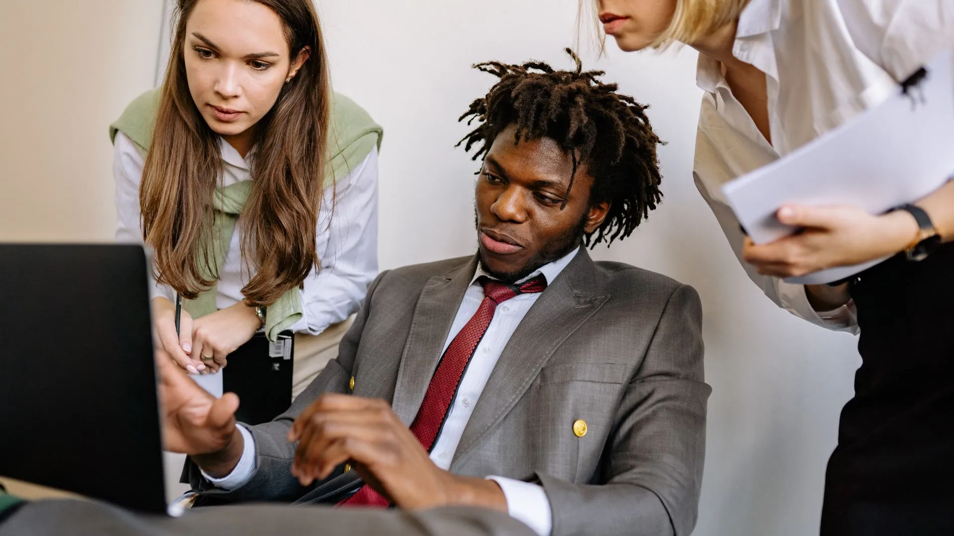 A manager is sitting at his computer, leading two of his team members through practical AI application. The two team members are standing behind him looking over his shoulder.