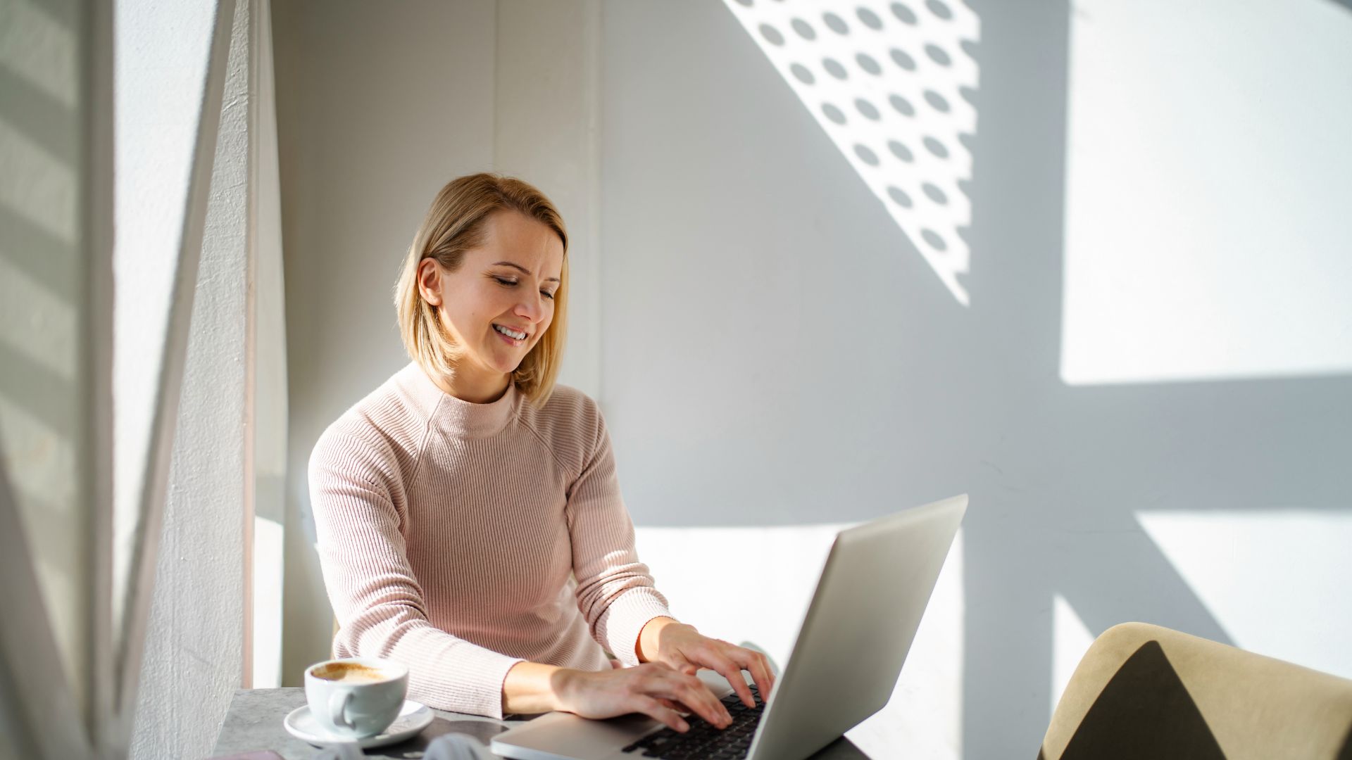 A woman is using AI on her laptop in a coffee shop.