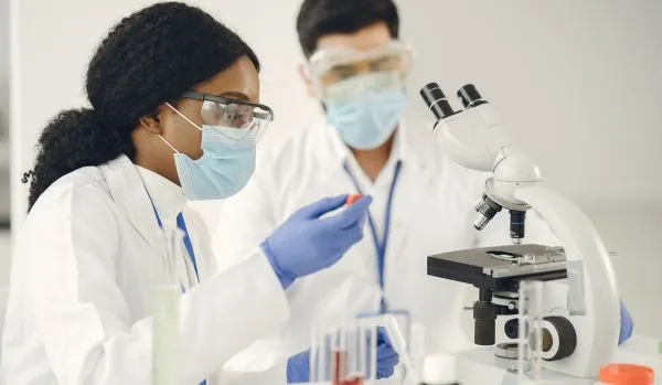 A man and woman are working with a microscope.