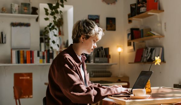 A person is sitting at a table in their apartment working on their laptop.