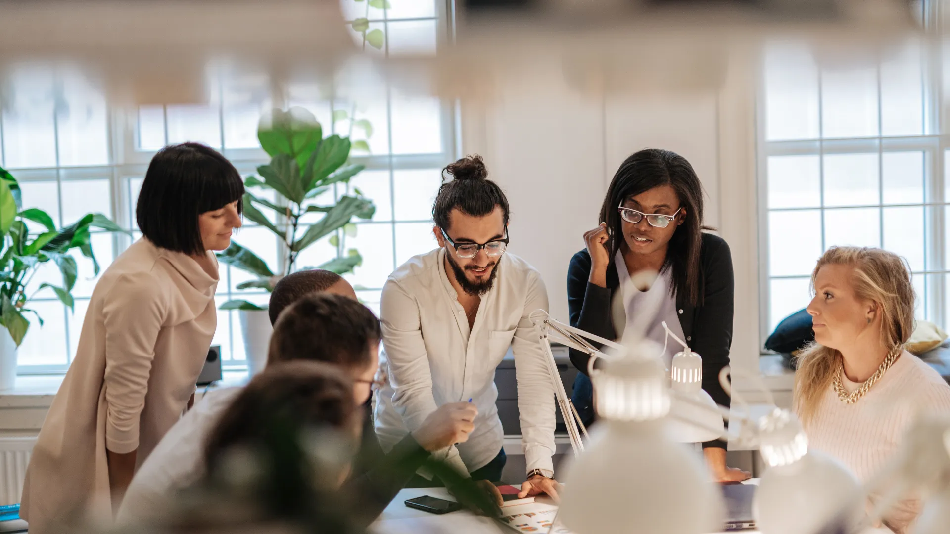 There are a group of seven people in an office gathered around a table working on an initiative.