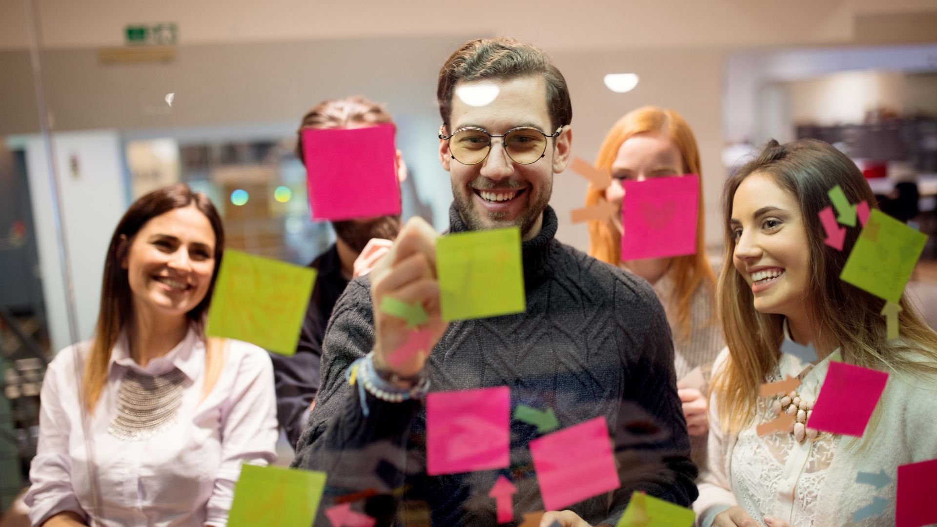 We are looking through a glass whiteboard at a team of people writing goals on postits and placing it on the white board.