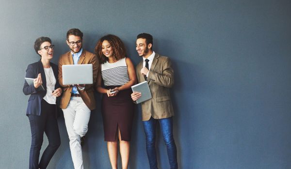 A group of four hispanic professionals are looking at a laptop and laughing.