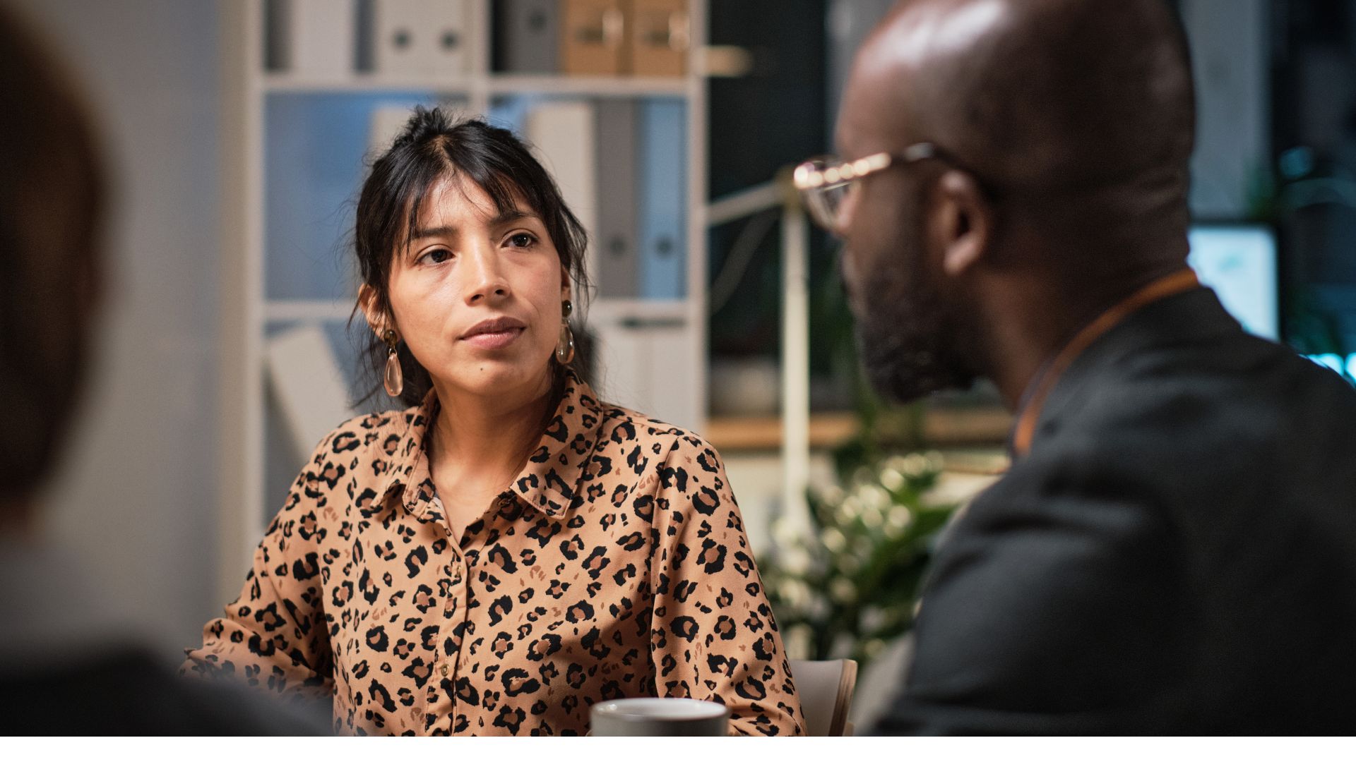 A woman wearing a leopard-print blouse attentively listens to a man during a discussion, exemplifying how she’s following a framework for receiving feedback in a professional setting.