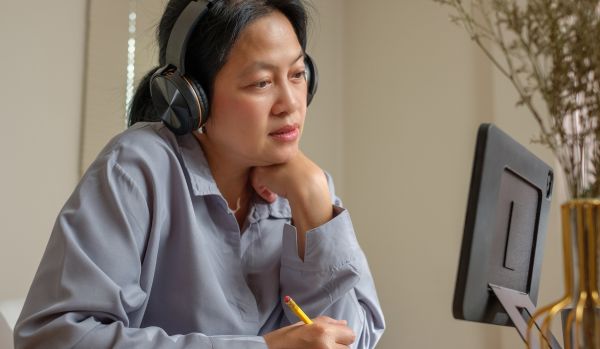 A woman with headphones looks at her computer monitor. She is participating in employee training.