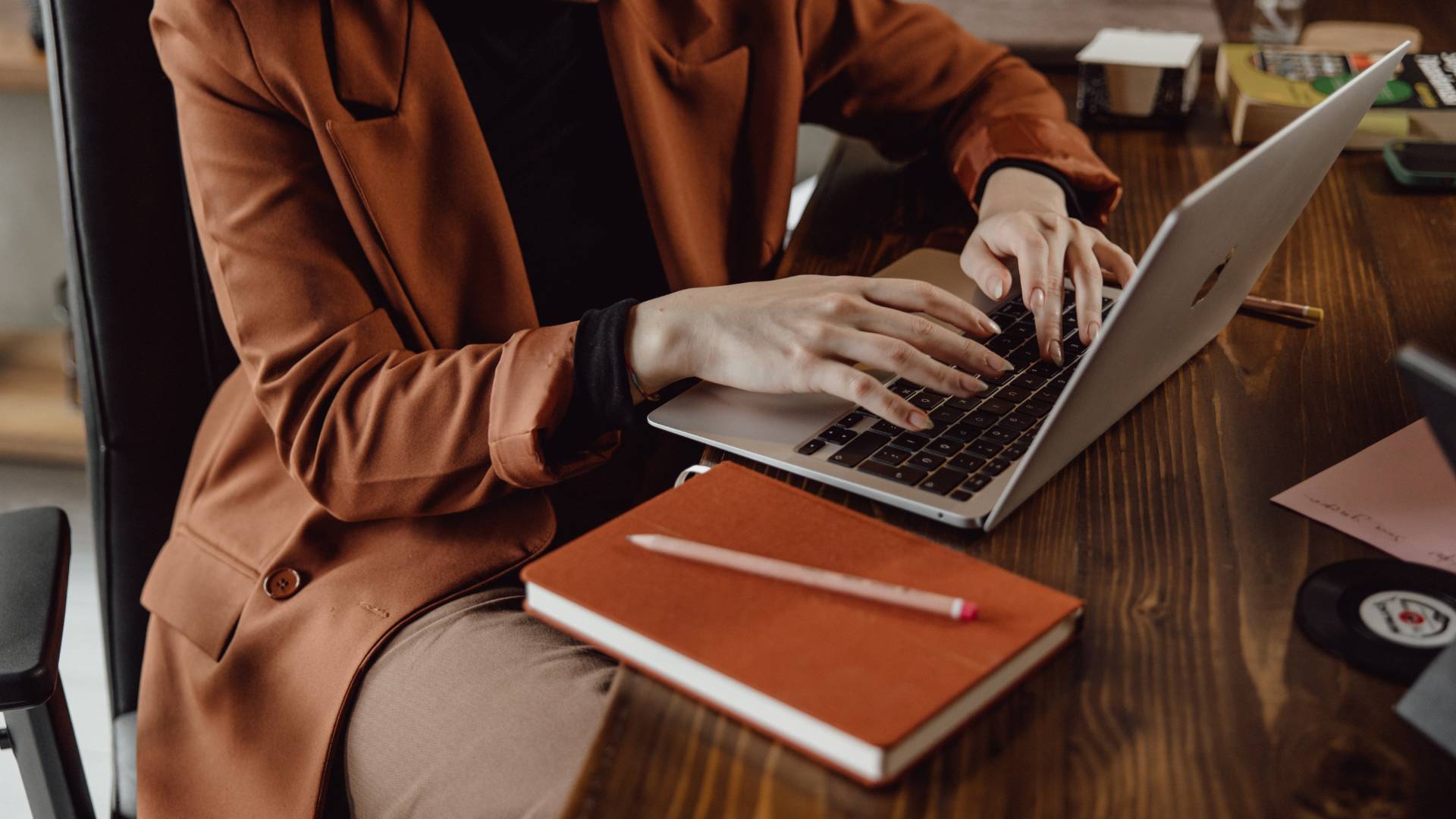 We are looking down at a woman sitting in a desk chair, typing on a laptop. We can only see her from the neck down.