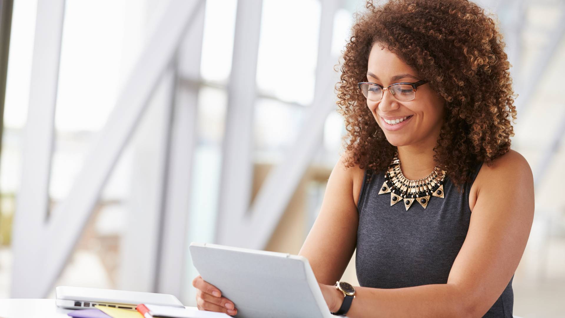 A woman is smiling down at her tablet in her office.