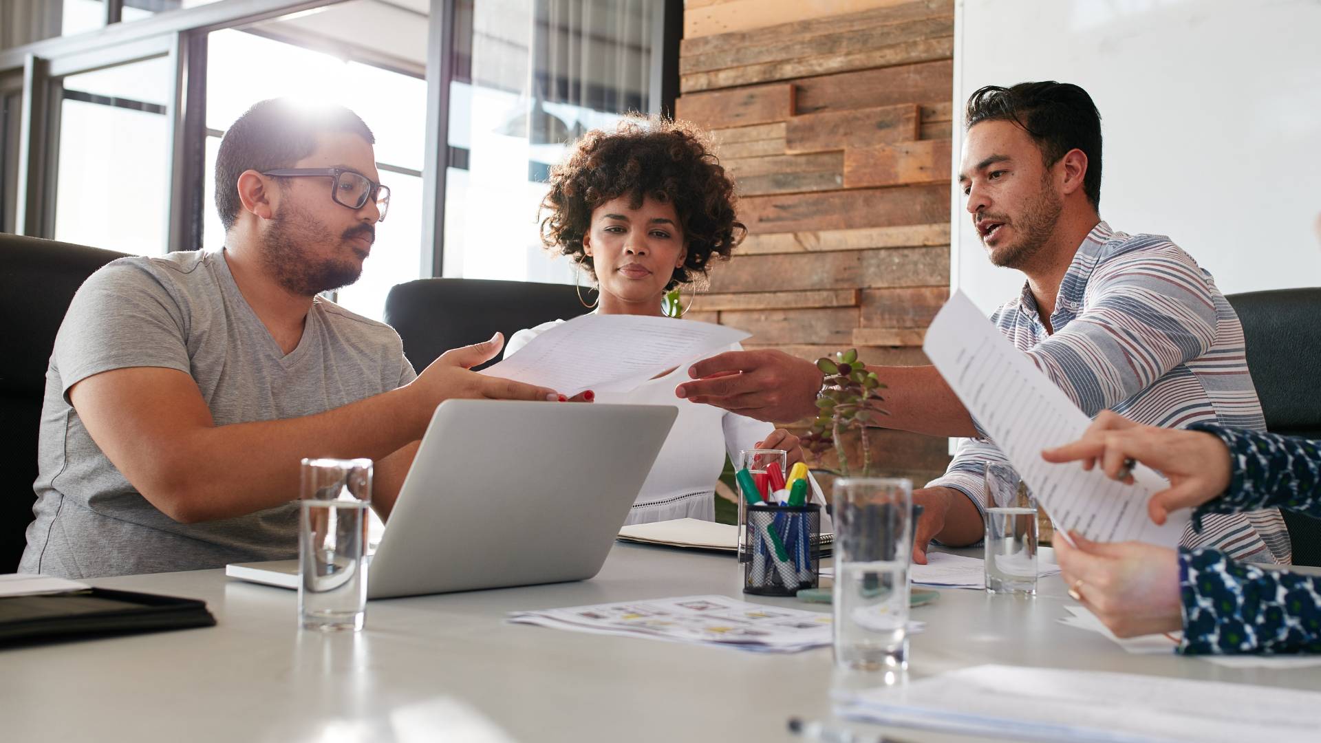 Three people are seated at a table looking over documents. There are two men and one woman in the middle. They have a laptop in front of them.