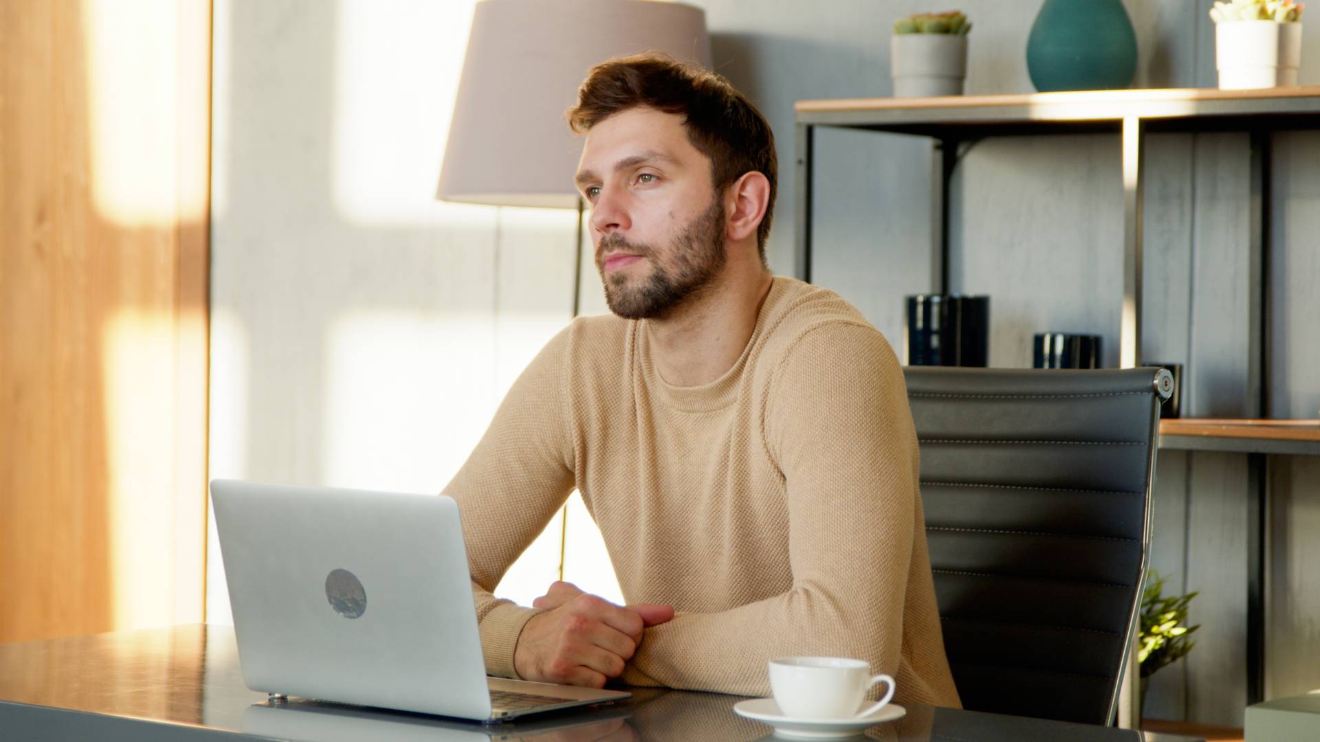 A man is working at his laptop, staring into the distance deep in thought.