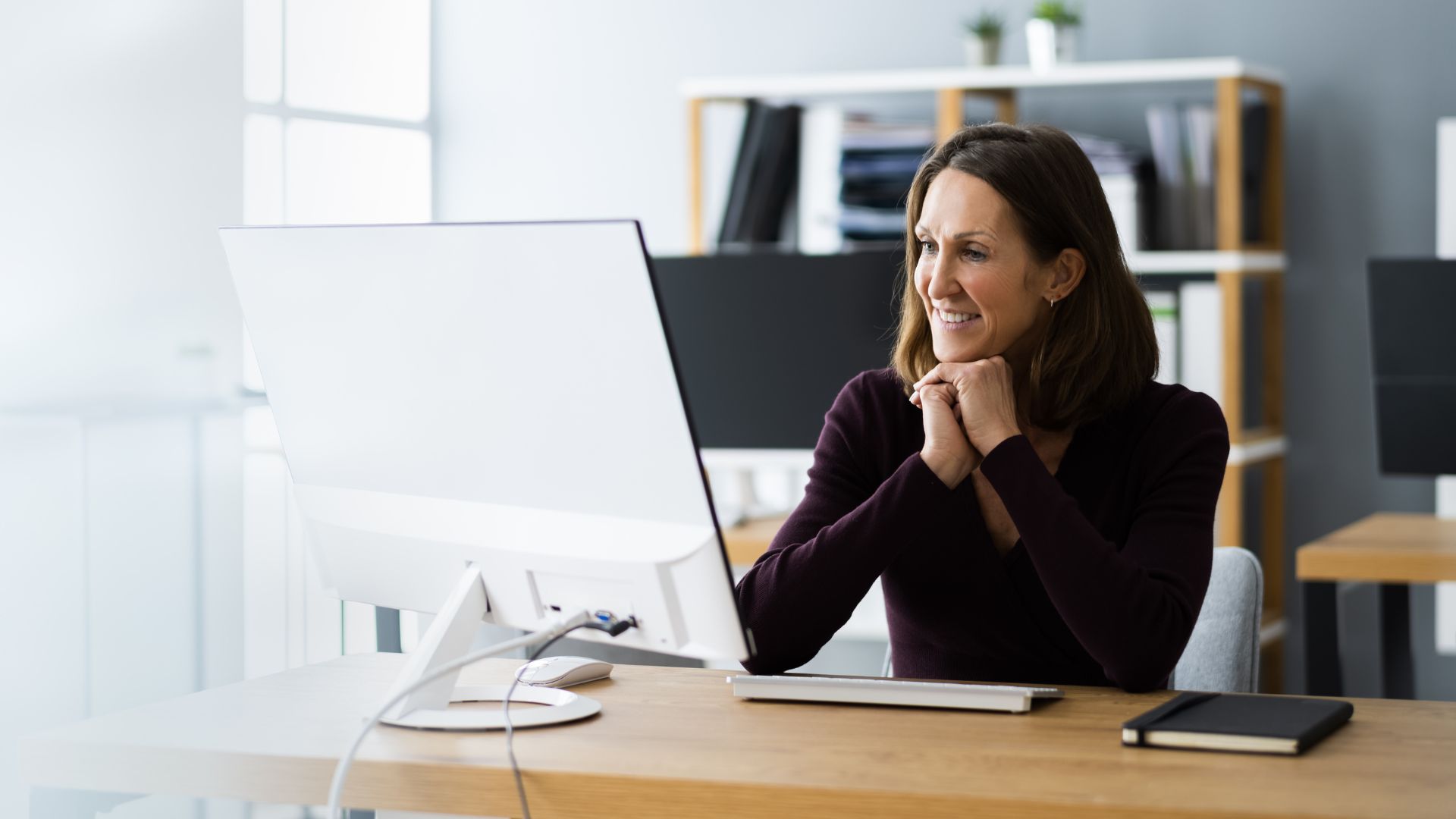 A female-presenting executive is working on a computer in her home office with a bookshelf behind her.