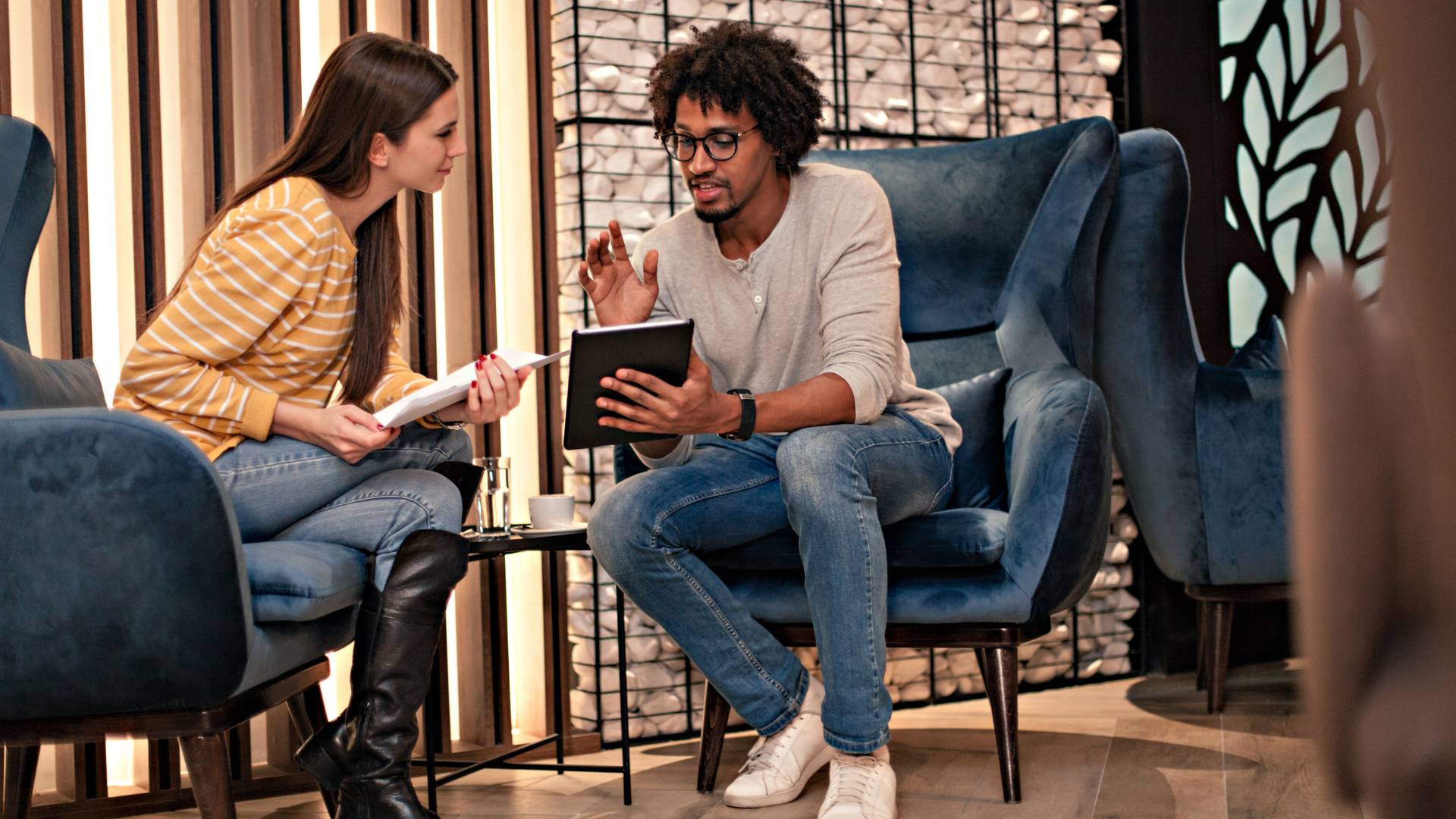 A man and a woman sit in a lobby looking at a tablet discussing career development.