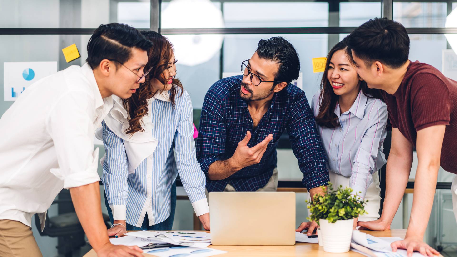 Five people standing around a table having a meeting. The manager is in the middle.