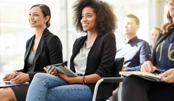 A group of professionals are sitting in a classroom-style training environment.
