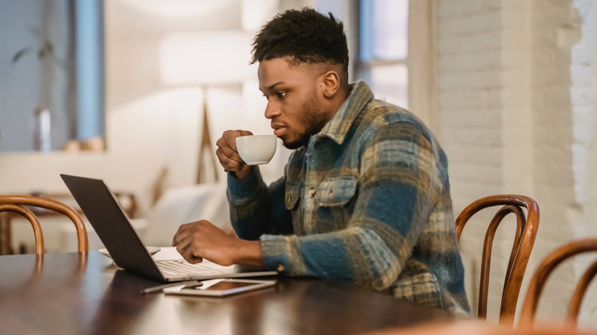 A young man sips his coffee while working on his laptop in a coffee shop