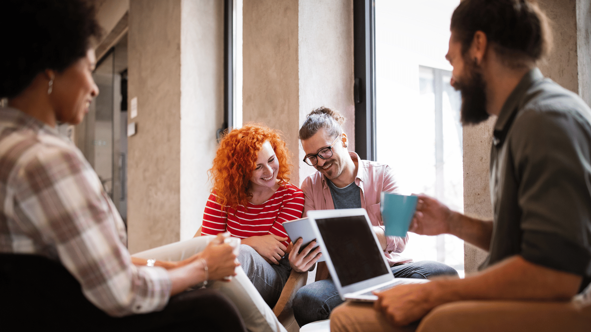 4 colleagues are collaborating in while sitting within common area of an office.