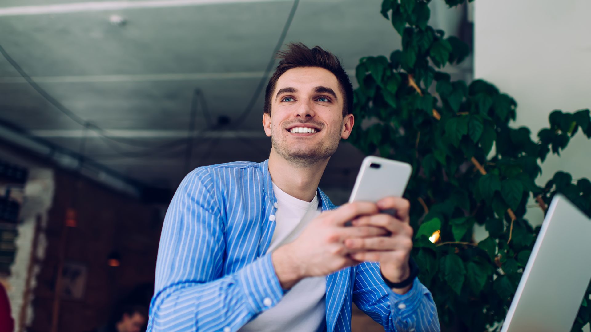 A young man is smiling off into the distance while holiday his phone in both hands.