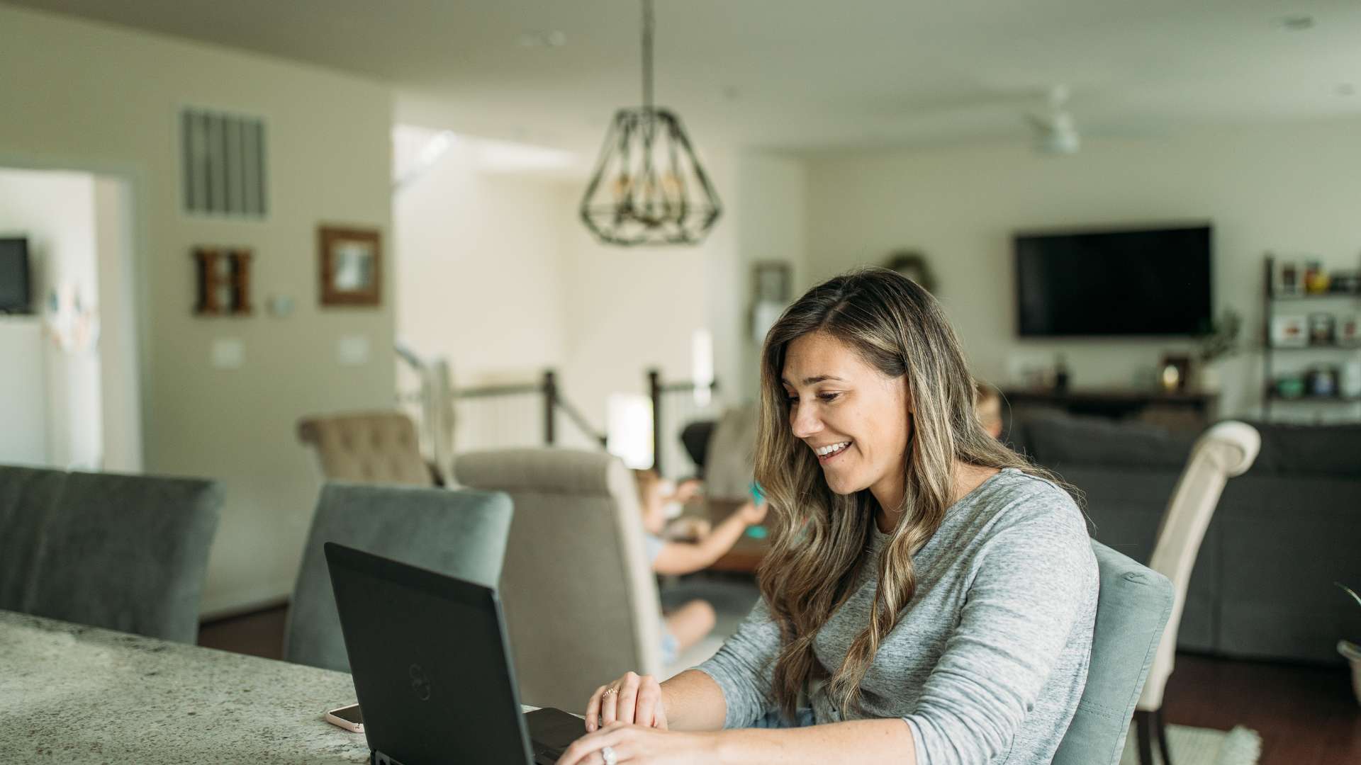 A woman in her early 40s works from her kitchen island. Behind her, her home is blurred.