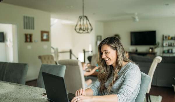 A woman in her early 40s works from her kitchen island. Behind her, her home is blurred.