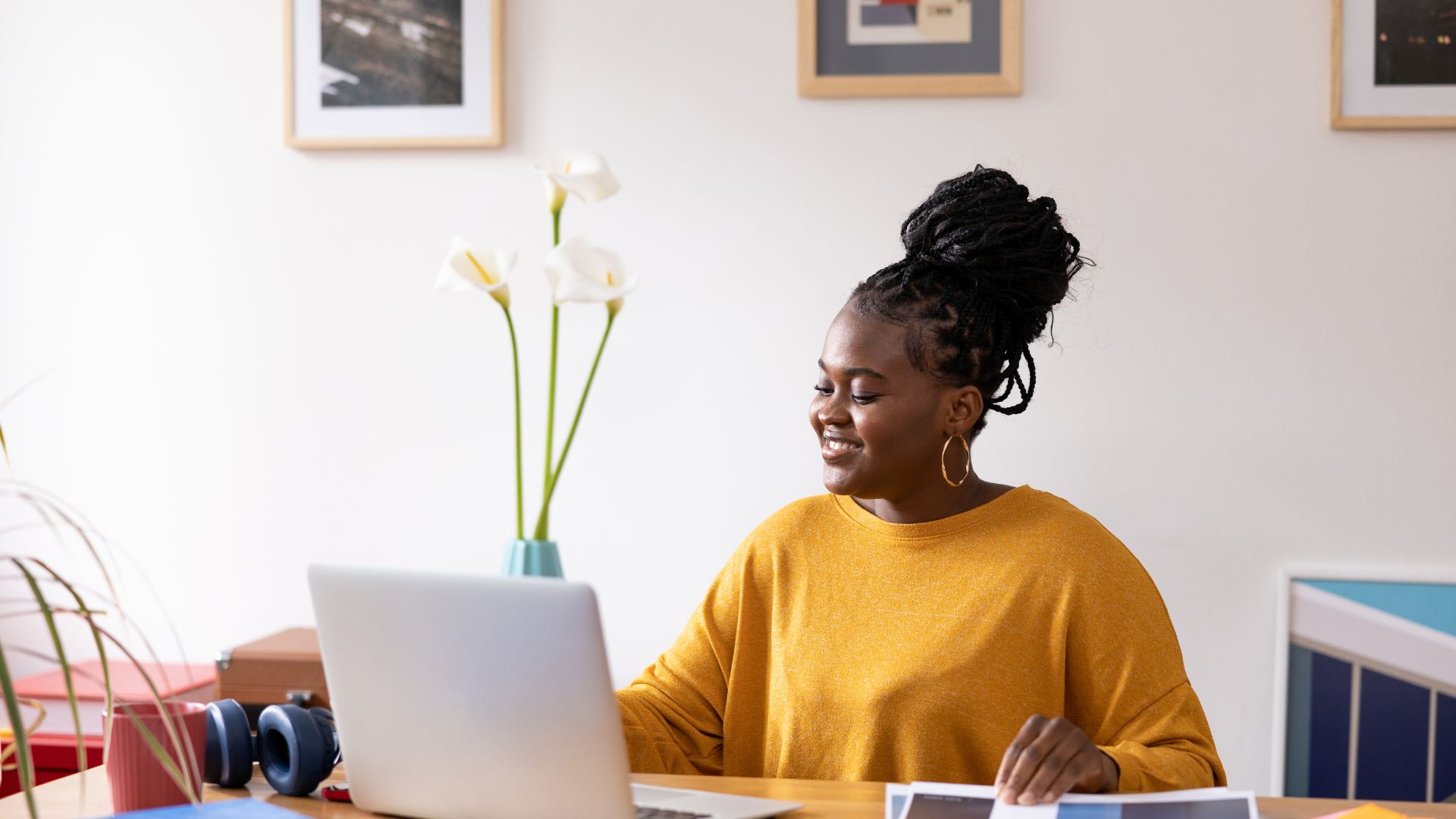 A young woman in a yellow shirt is working on her laptop in her home office.