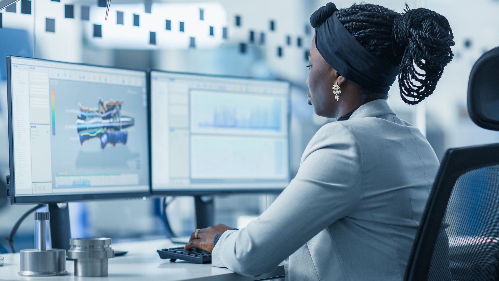 We're looking over the should of a woman who is working with AI on two computer screens.