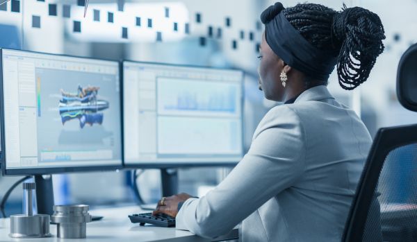 We're looking over the should of a woman who is working with AI on two computer screens.