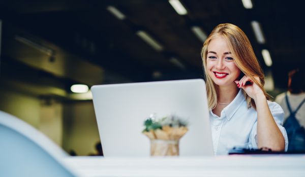 A young woman is smiling down at her laptop while working in a coworking space.