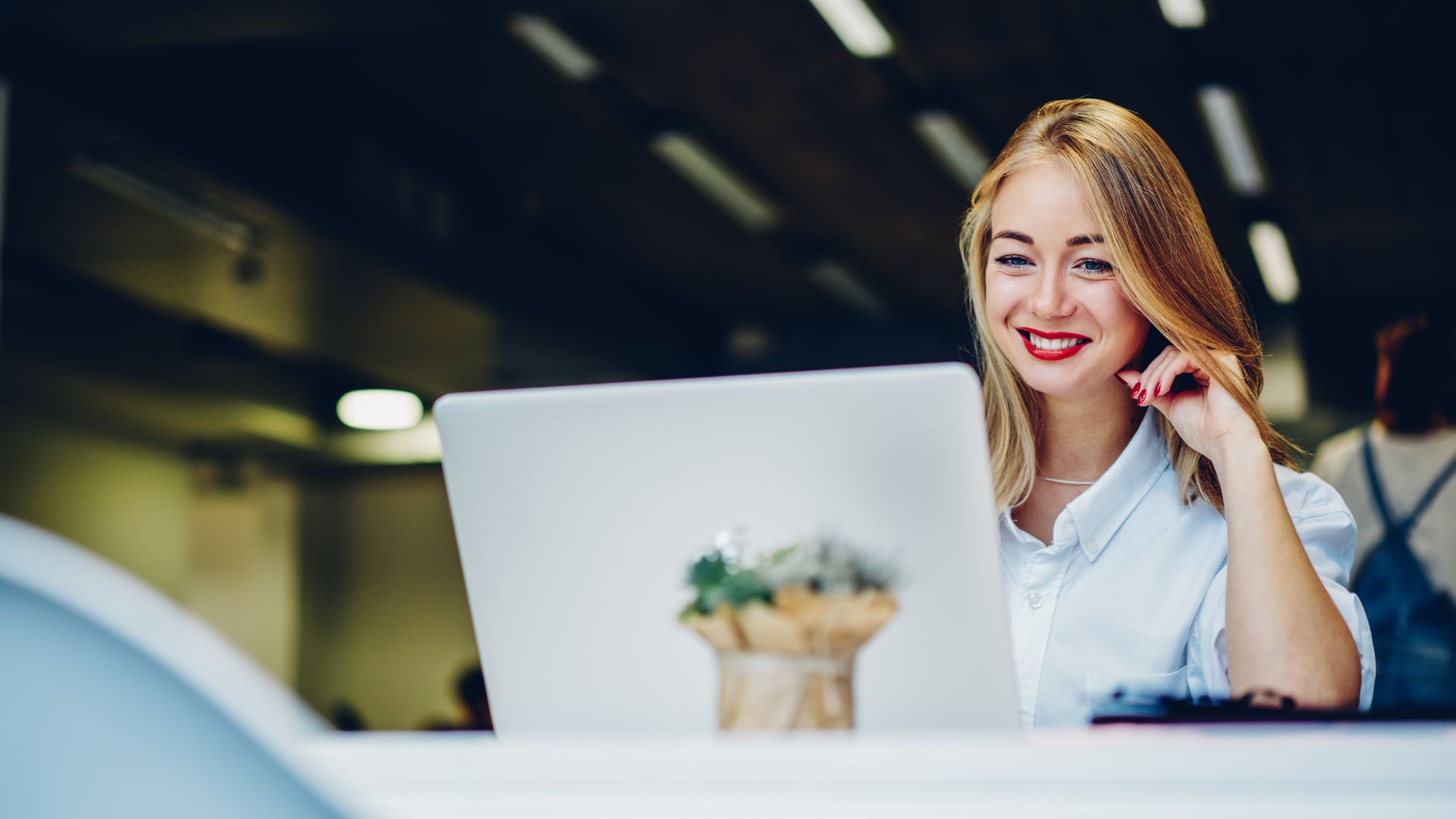 A young woman is smiling down at her laptop while working in a coworking space.
