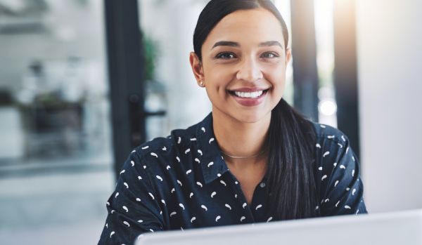 A young woman is smiling over the laptop at the camera.