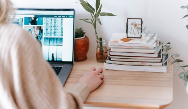 We are looking over a woman's shoulder as she uses her laptop on her desk at home.