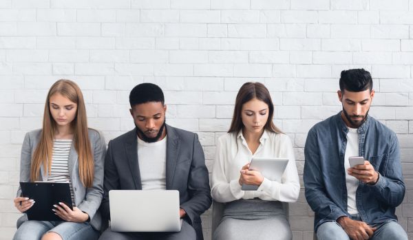 A group of 4 diverse technology professionals are sitting in a row, preparing for a job interview on their personal devices.