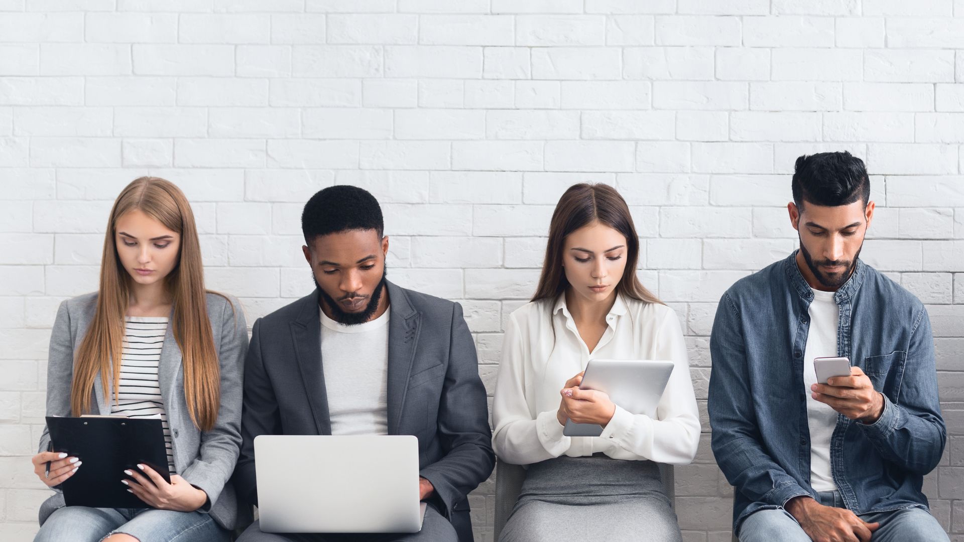 A group of 4 diverse technology professionals are sitting in a row, preparing for a job interview on their personal devices.