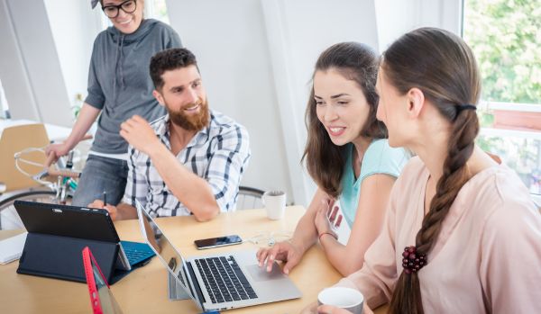A happy team of people are experimenting with AI in their office on their laptops.