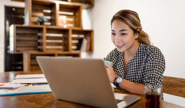 A young woman is working from home. She's smiling at her laptop.