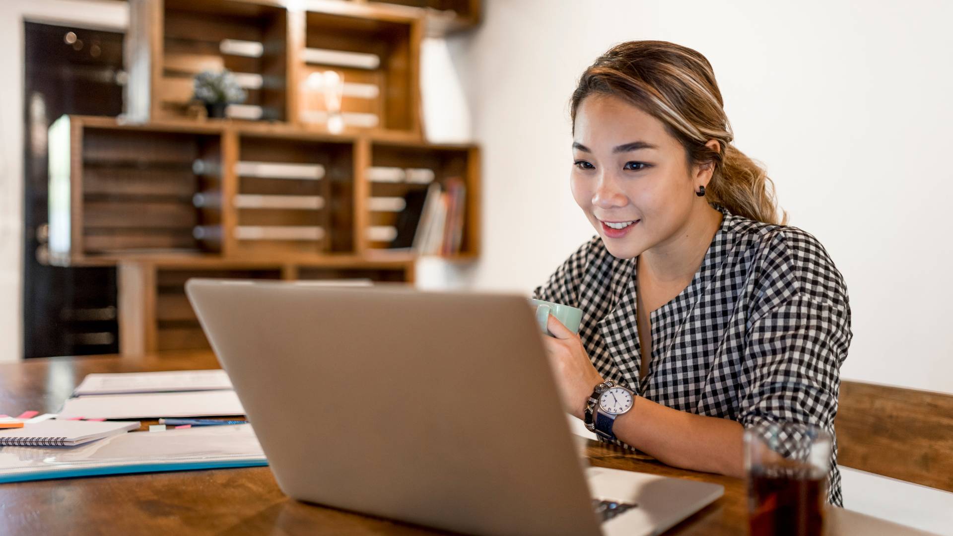 A young woman is working from home. She's smiling at her laptop.