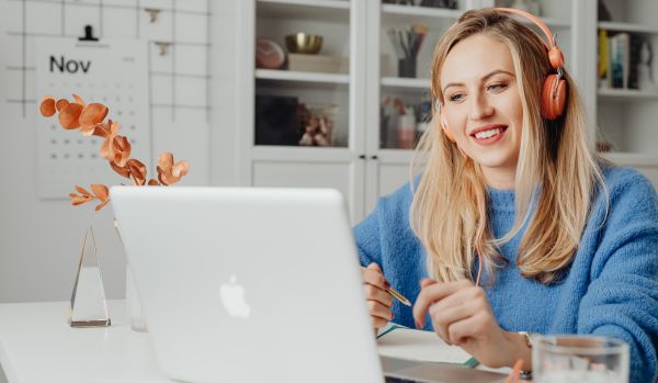 A young woman is working from her kitchen on her laptop with headphones on.