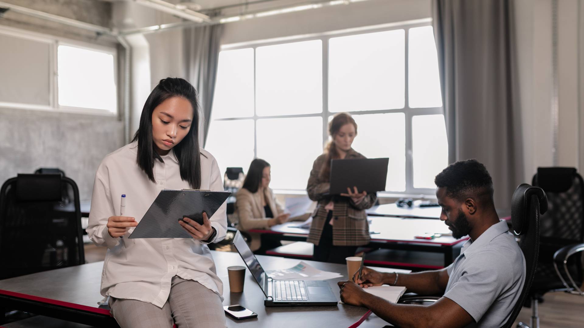 There are four employees staggered around an office on their laptops, working.