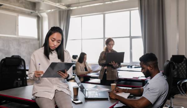 There are four employees staggered around an office on their laptops, working.