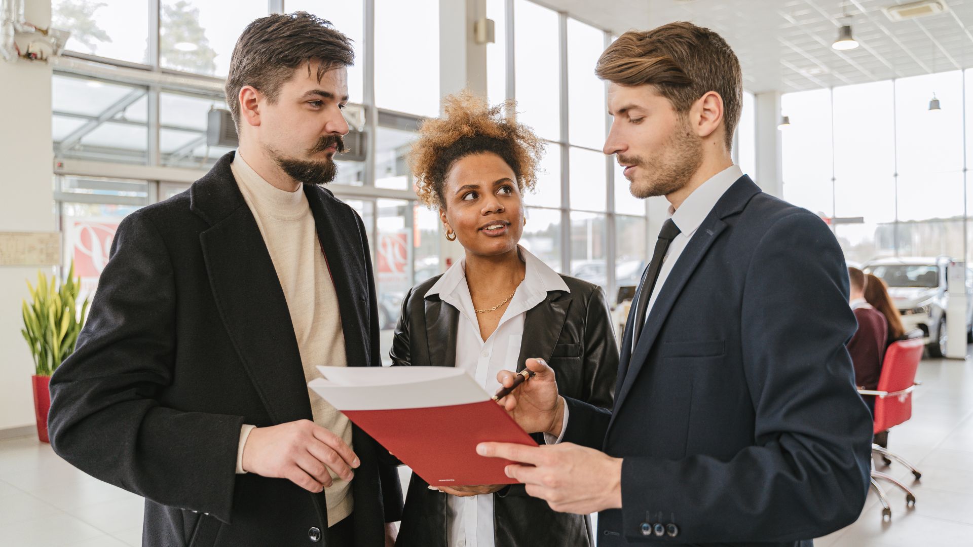 three colleagues are standing in a bright, open workspace discussing some documents one of them is holding.