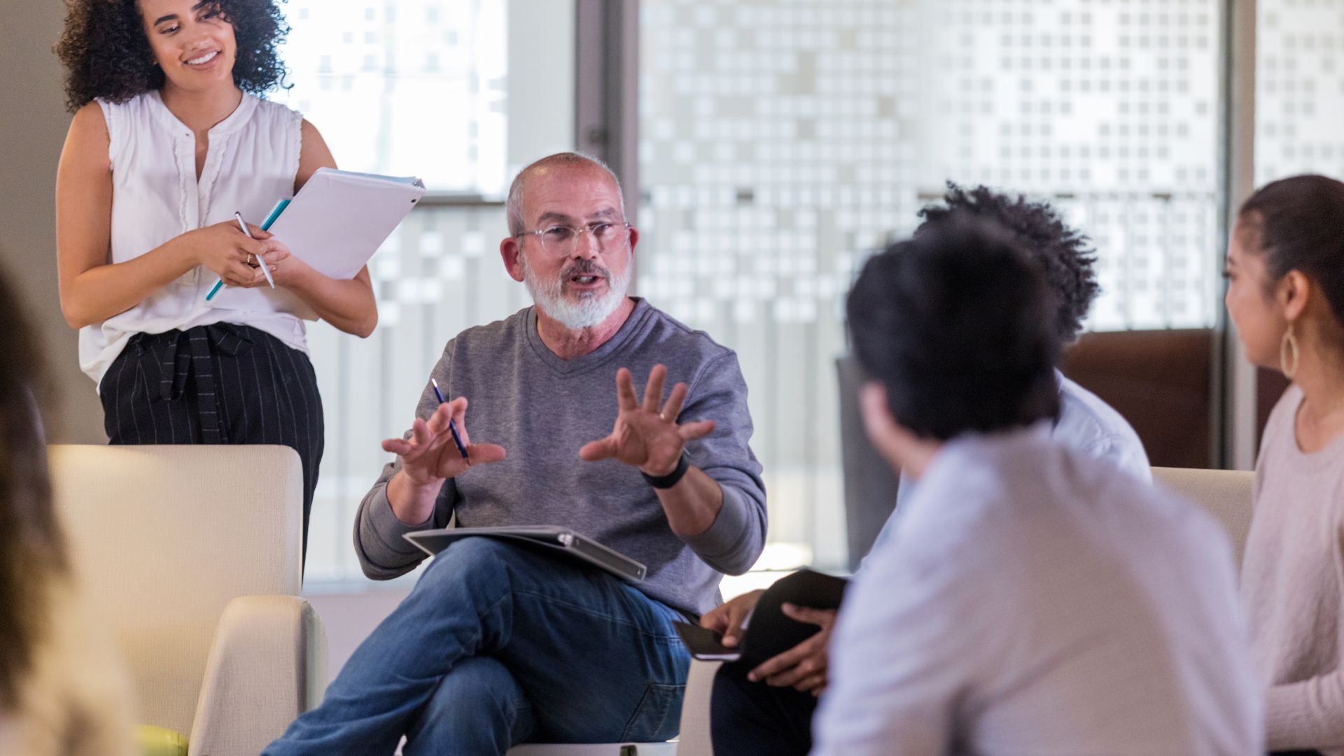 A man is leading a group of people in a change management training. The people are sitting in a circle of chairs.