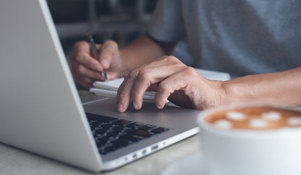A close-up photo of someone's hands on their laptop with a cup of coffee in the foreground.