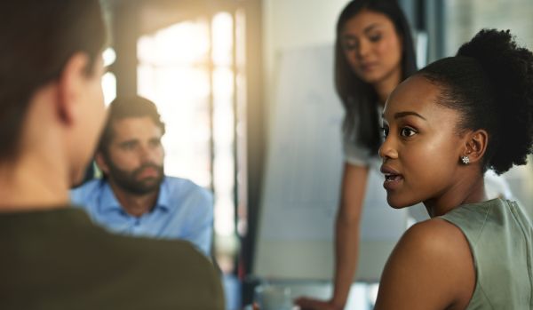 A group of four diverse employees are having a conversation in a conference room.