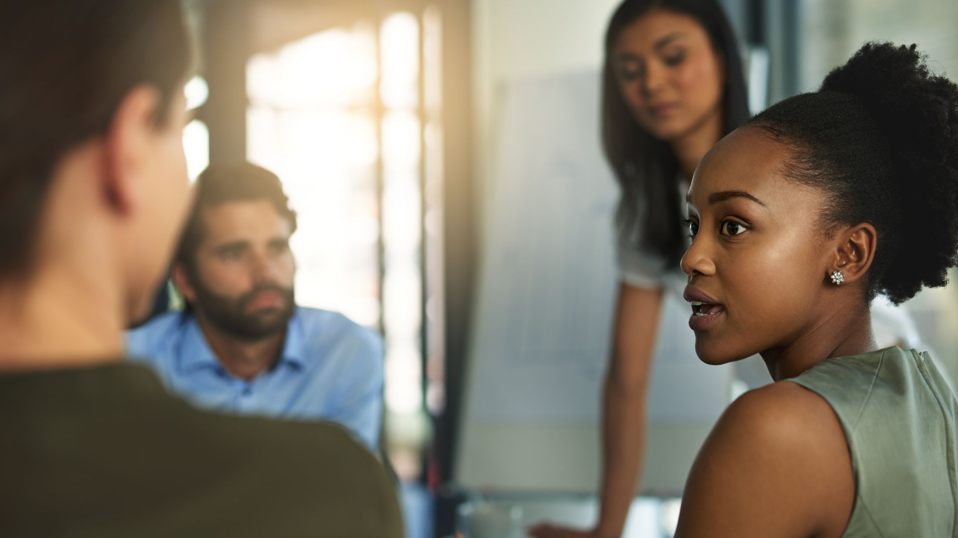 A group of four diverse employees are having a conversation in a conference room.