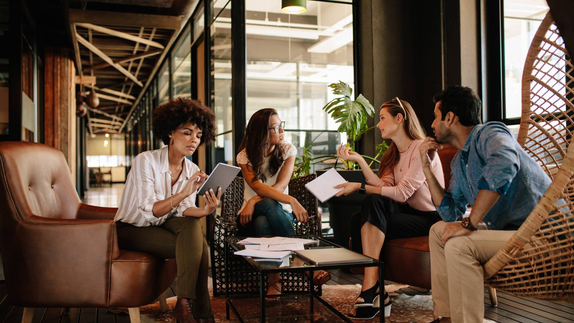 A diverse group of employees are sitting around a coffee table in a common area discussing a project.