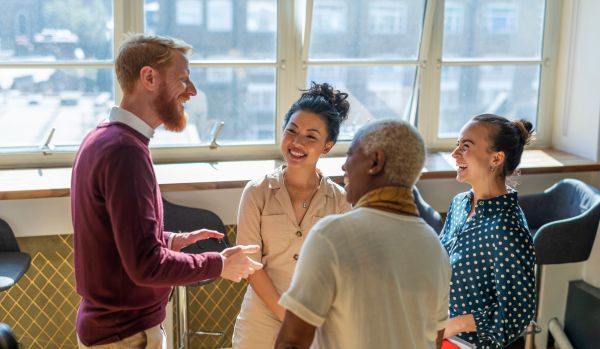 A diverse group of colleagues are standing in a common space, laughing and talking.