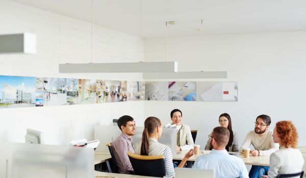 A diverse team of people are sitting around a table in a minimalist, modern office having a group conversation.