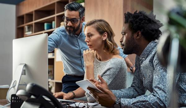 A diverse group of people are working together, looking at a computer monitor.