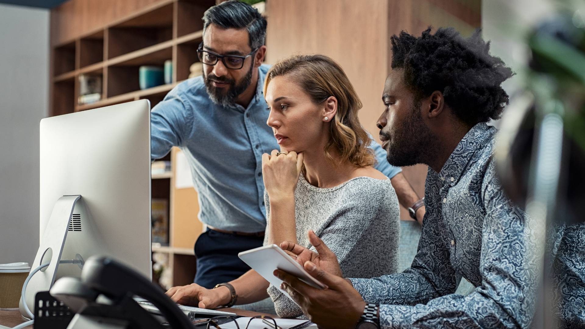 A diverse group of people are working together, looking at a computer monitor.