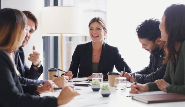 A diverse group of professionals are talking and laughing around a conference table.
