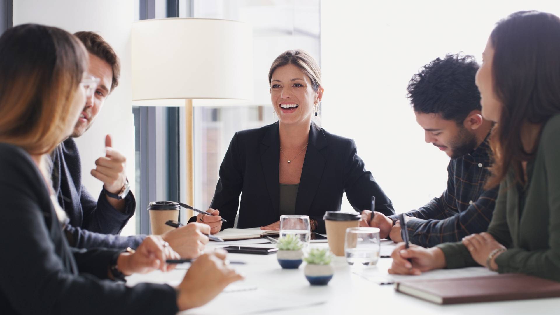 A diverse group of professionals are talking and laughing around a conference table.